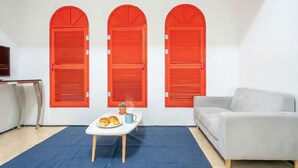 A room with a white sofa, a small table with a plant and a plate of food, and three red shutters on the wall. - Chuncheon Vishop Pension (Chuncheon)