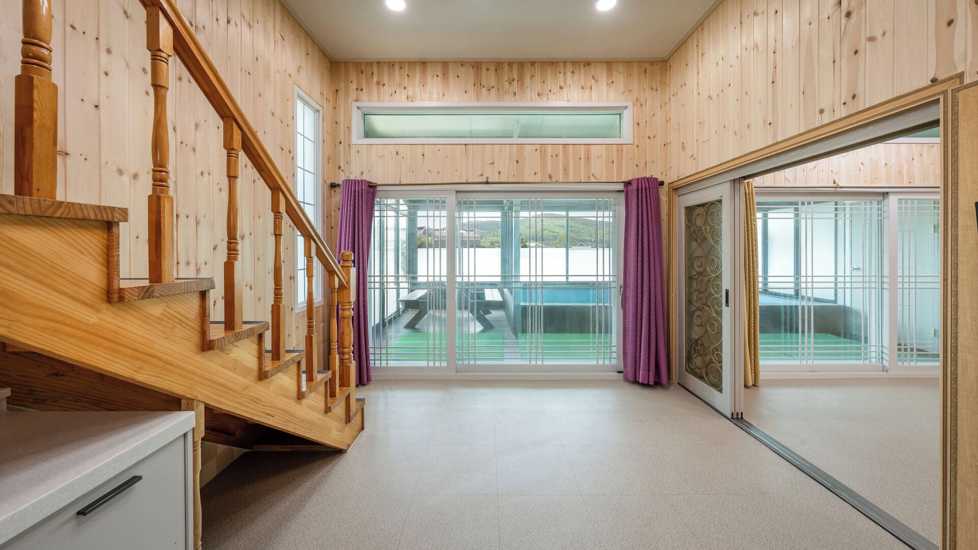 Un intérieur en bois avec un escalier, de grandes portes-fenêtres coulissantes et une vue sur l’extérieur.