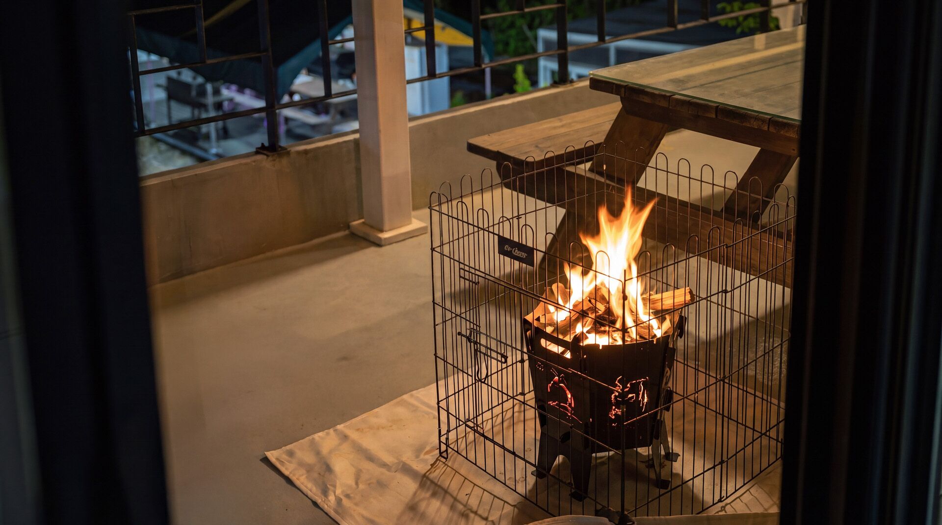 A metal fire pit with flames, surrounded by a metal fence, on a concrete floor.