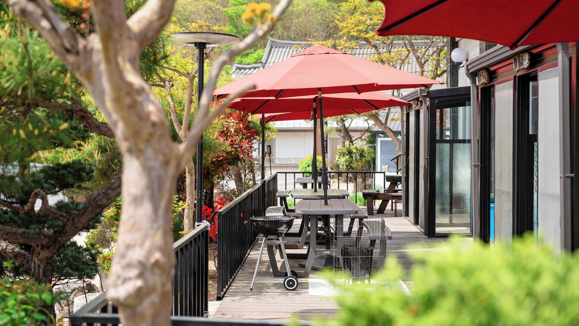 An outdoor patio with tables and chairs, red umbrellas, and a grill.