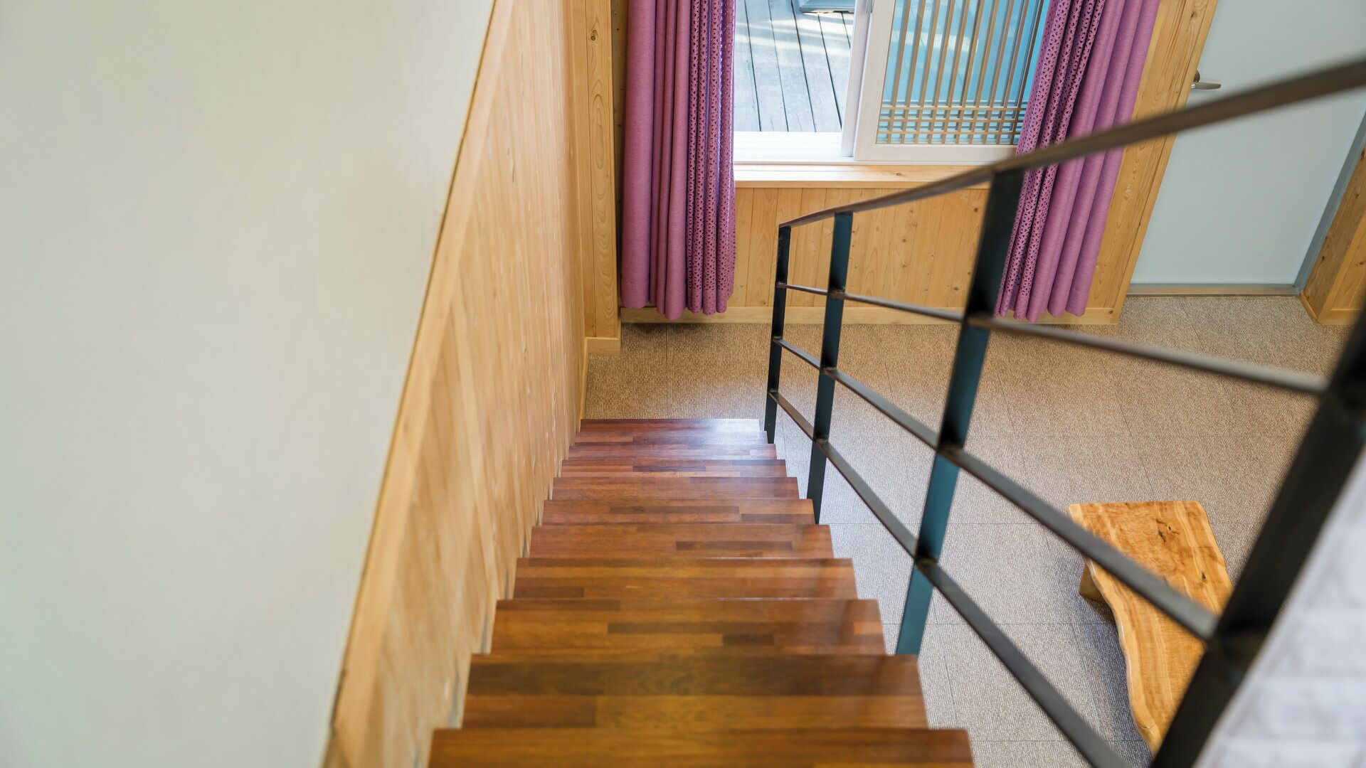 A wooden staircase with a metal railing leading to a room with a window and purple curtains.