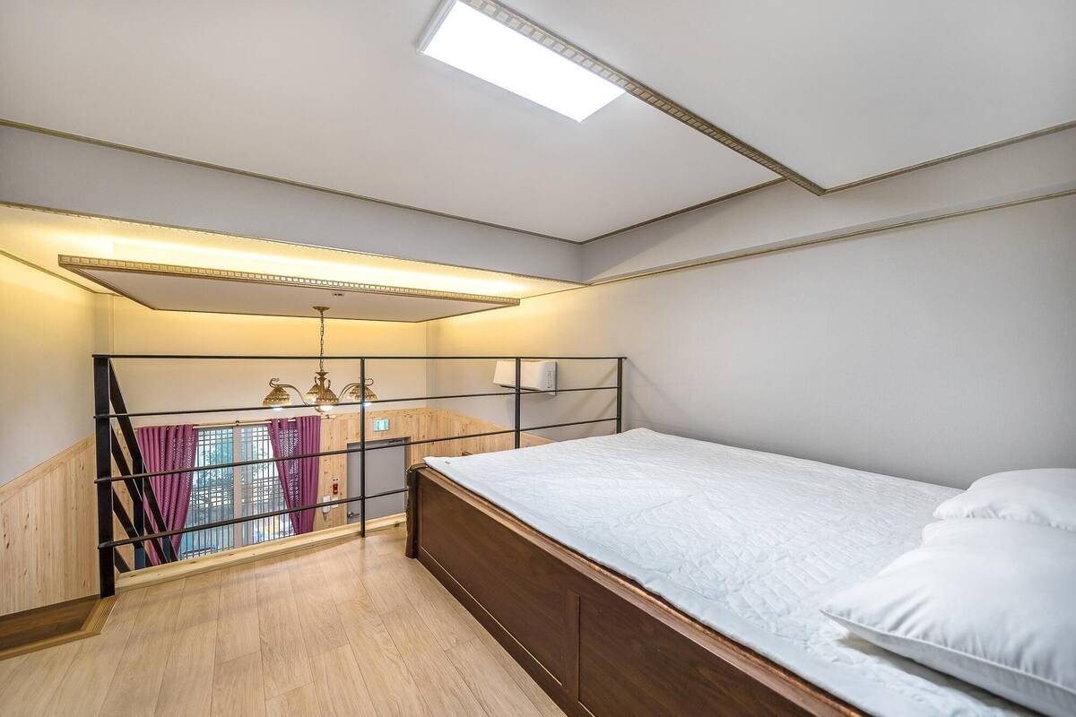 Une chambre avec un puits de lumière, un lit, un plancher en bois et une vue sur un balcon.