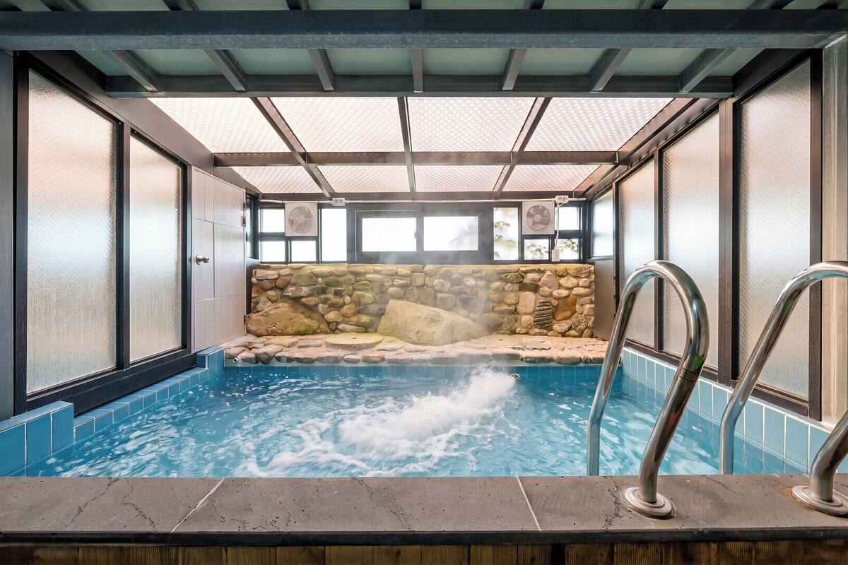 Une piscine intérieure avec un mur en pierre, une terrasse en bois et un escalier en métal.