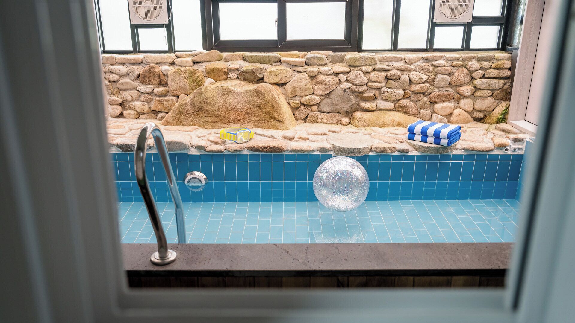 Un muro de piedra, una piscina con azulejos azules y una ventana con vistas al cielo.