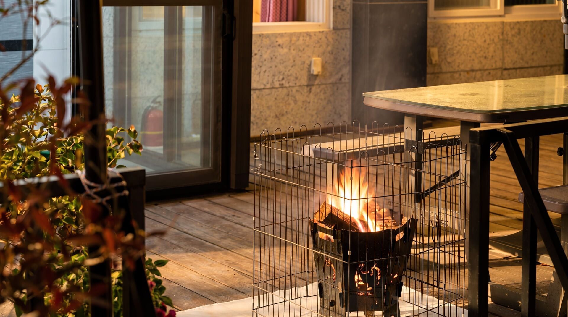 Eine Terrassenfläche mit Tisch, Feuerstelle und Blick durch eine Glastür.