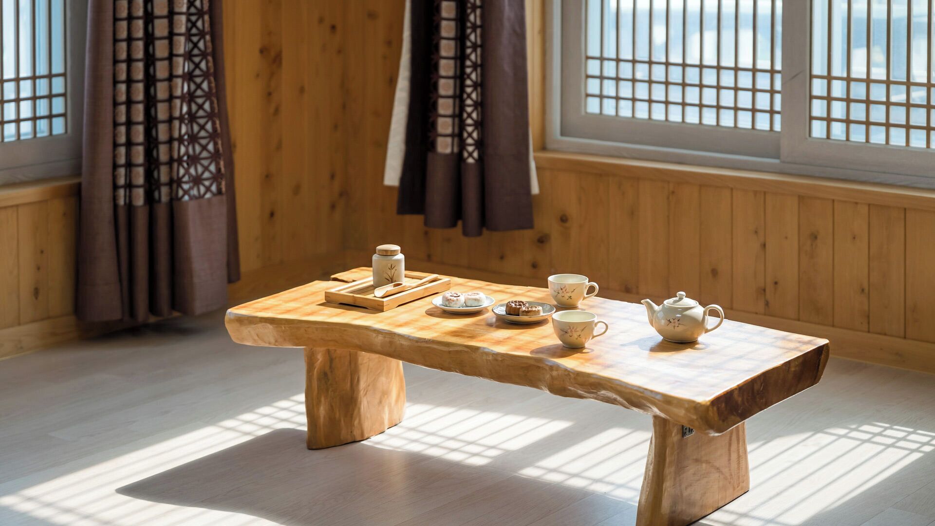A wooden table with tea set and pastries, set in a room with wooden walls and windows.