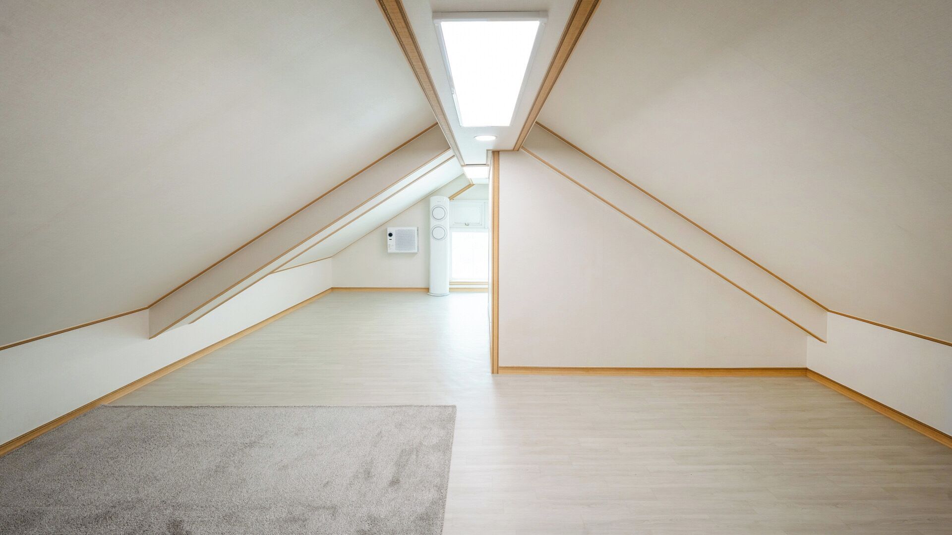 A spacious attic room with a sloped ceiling, a large skylight, and a visible air conditioning unit.