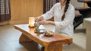 A person pouring tea into a cup on a wooden table with a lantern and pastries. - Gyeongju Soraedanga Pension (Gyeongju)
