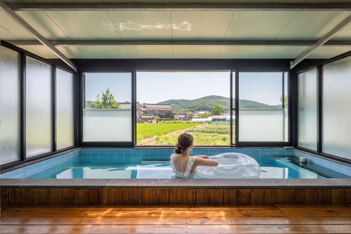 Une personne se détend dans un bain à remous, avec vue sur un bâtiment traditionnel et une végétation luxuriante.