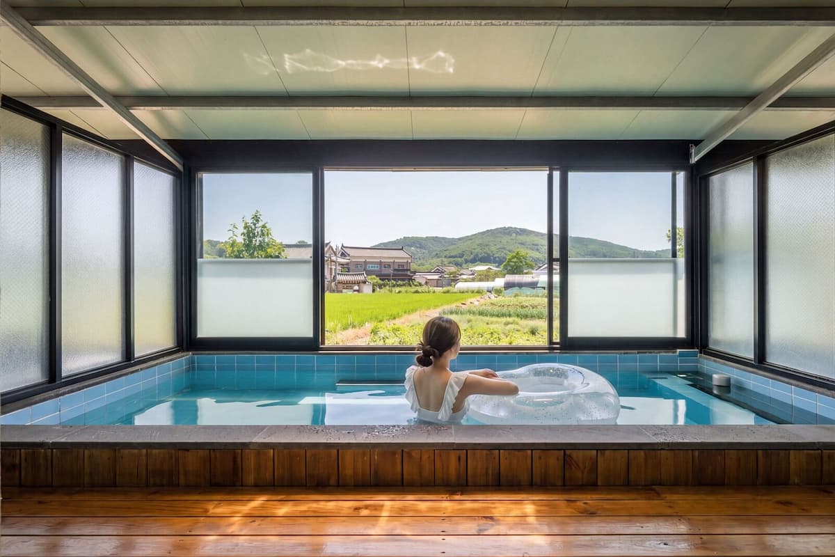 A person relaxing in a hot tub with a view of a traditional building and greenery.