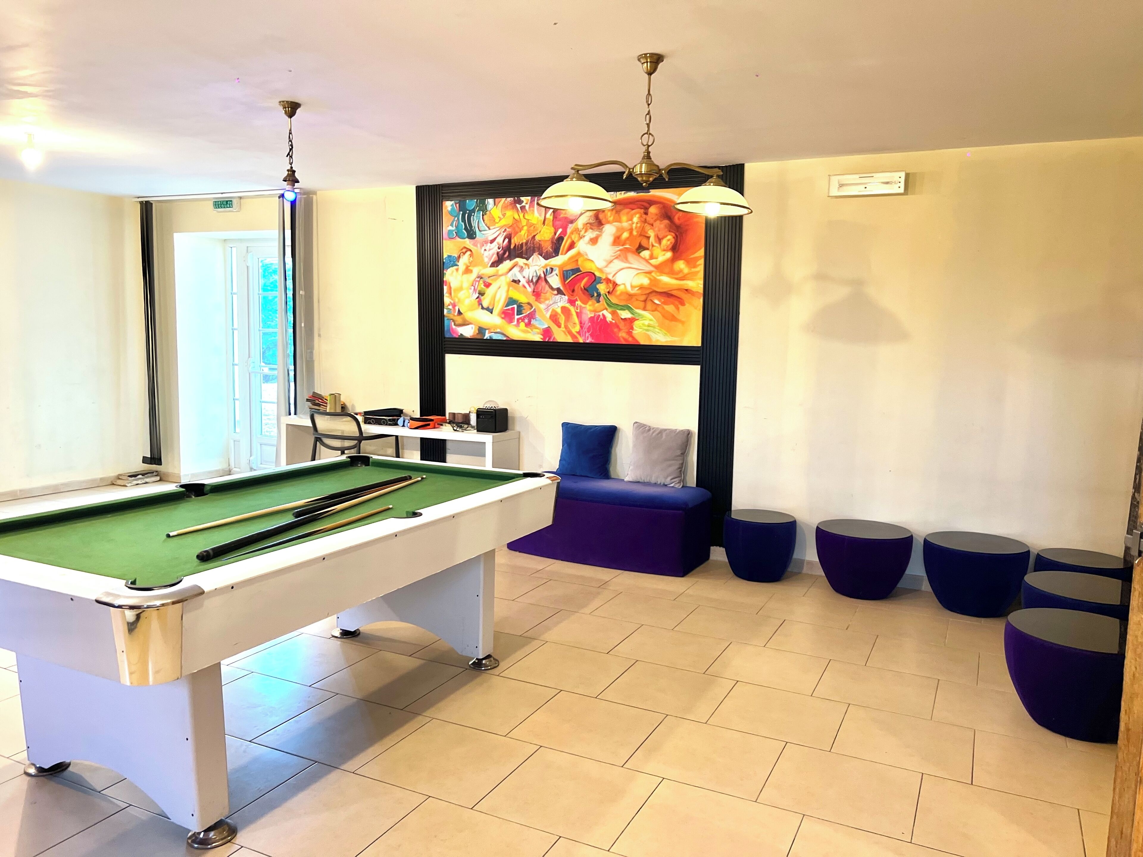 Ein Billardtisch mit Billardstöcken, eine Couch und ein farbenfrohes Bild an der Wand.