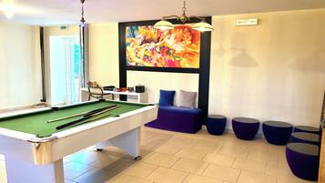 Ein Billardtisch mit Billardstöcken, eine Couch und ein farbenfrohes Bild an der Wand.