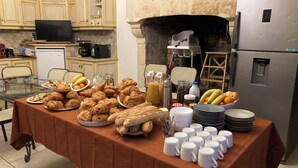 A breakfast buffet with pastries, fruits, and coffee in a kitchen with stone walls and modern appliances.