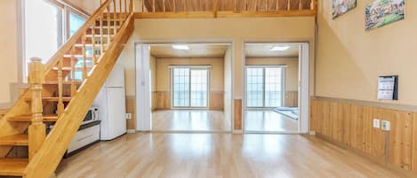 A spacious interior with a wooden staircase, large sliding glass doors, and a high ceiling.
