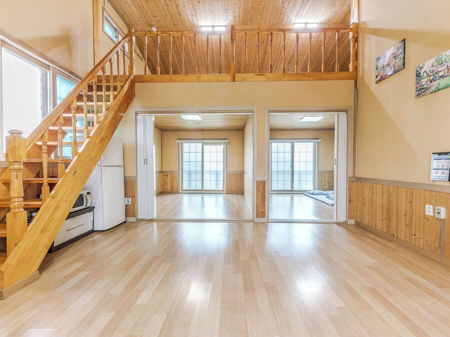 A spacious interior with a wooden staircase, large sliding glass doors, and a high ceiling.