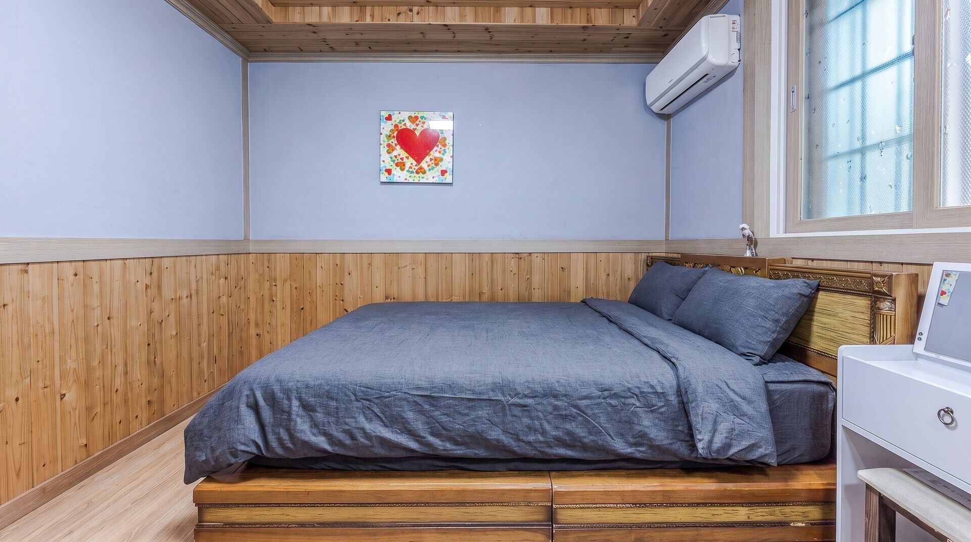 Un dormitorio con estructura de cama de madera, colcha gris y un aire acondicionado de pared.