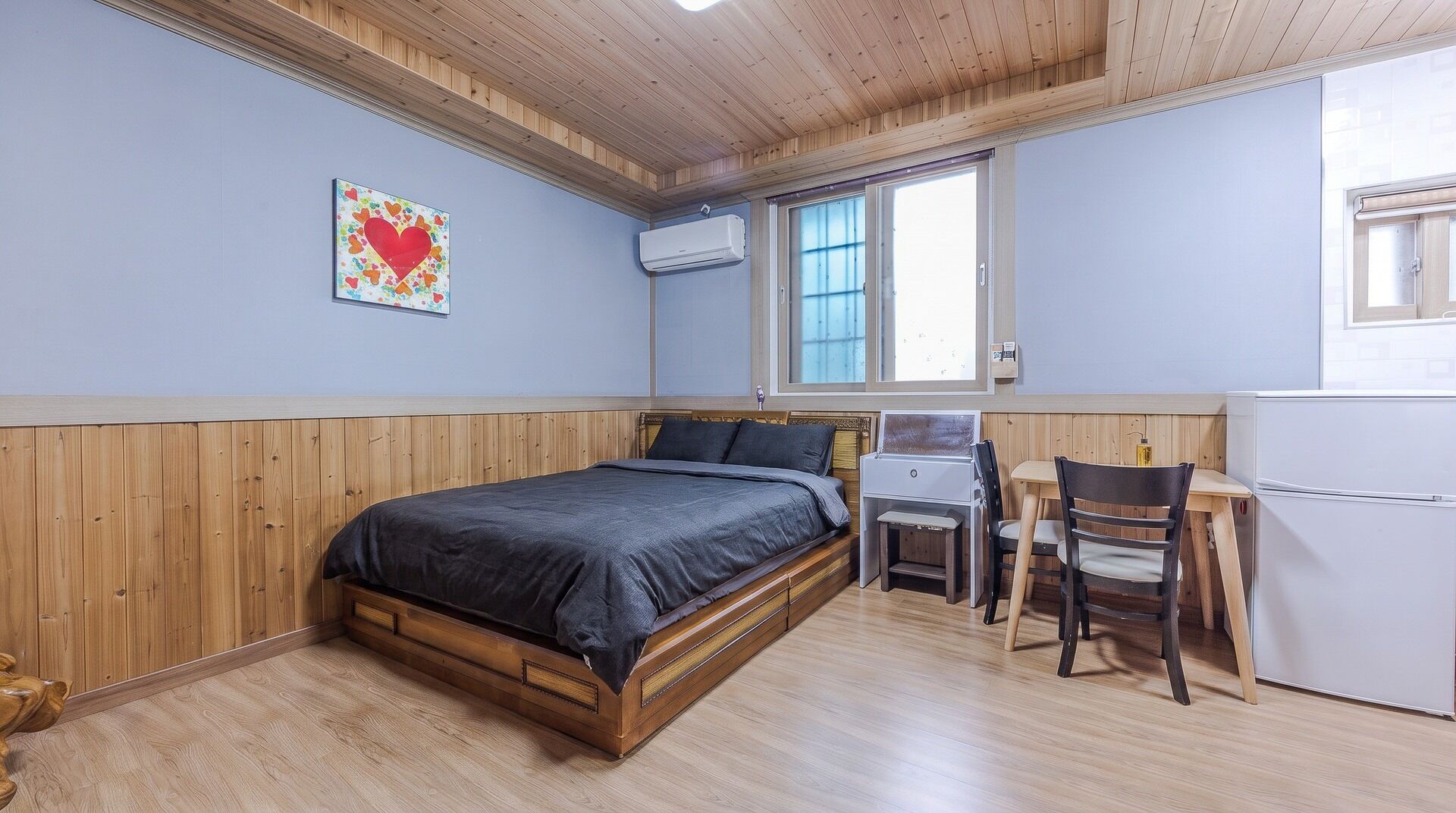 Un dormitorio con una cama de madera, un escritorio con una silla, una ventana y un equipo de aire acondicionado.