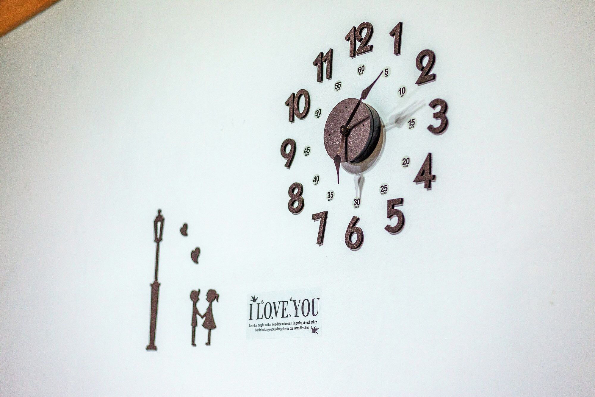 Un reloj de pared con un diseño decorativo, que incluye un corazón y una pareja tomados de la mano, con la frase 'I LOVE YOU' y una cita debajo.