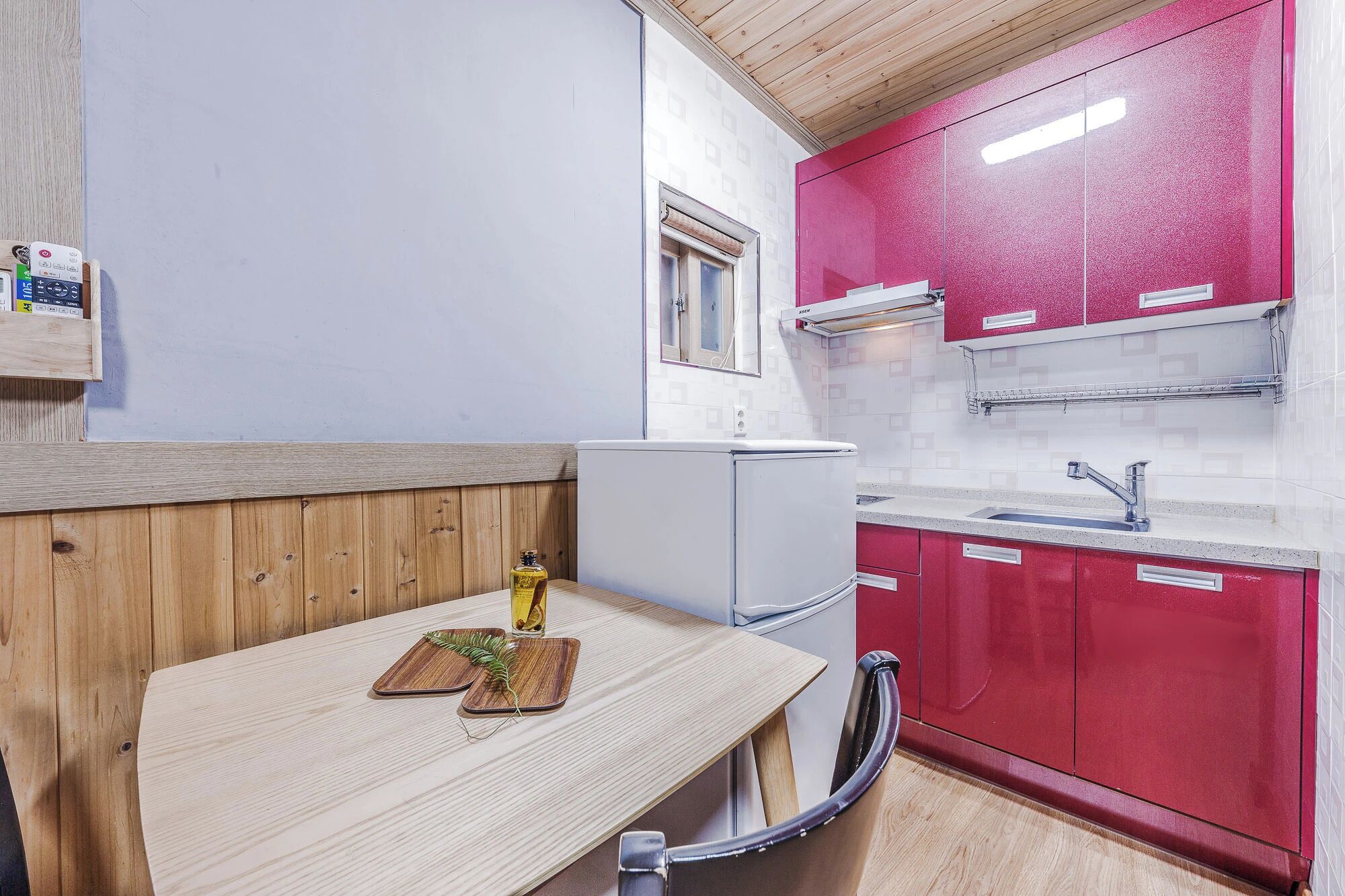 Una cocina compacta con refrigerador, pileta y una mesa de madera con posavasos.