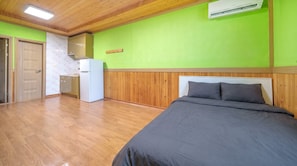 A room with a bed, a refrigerator, a wooden ceiling, and a green wall.