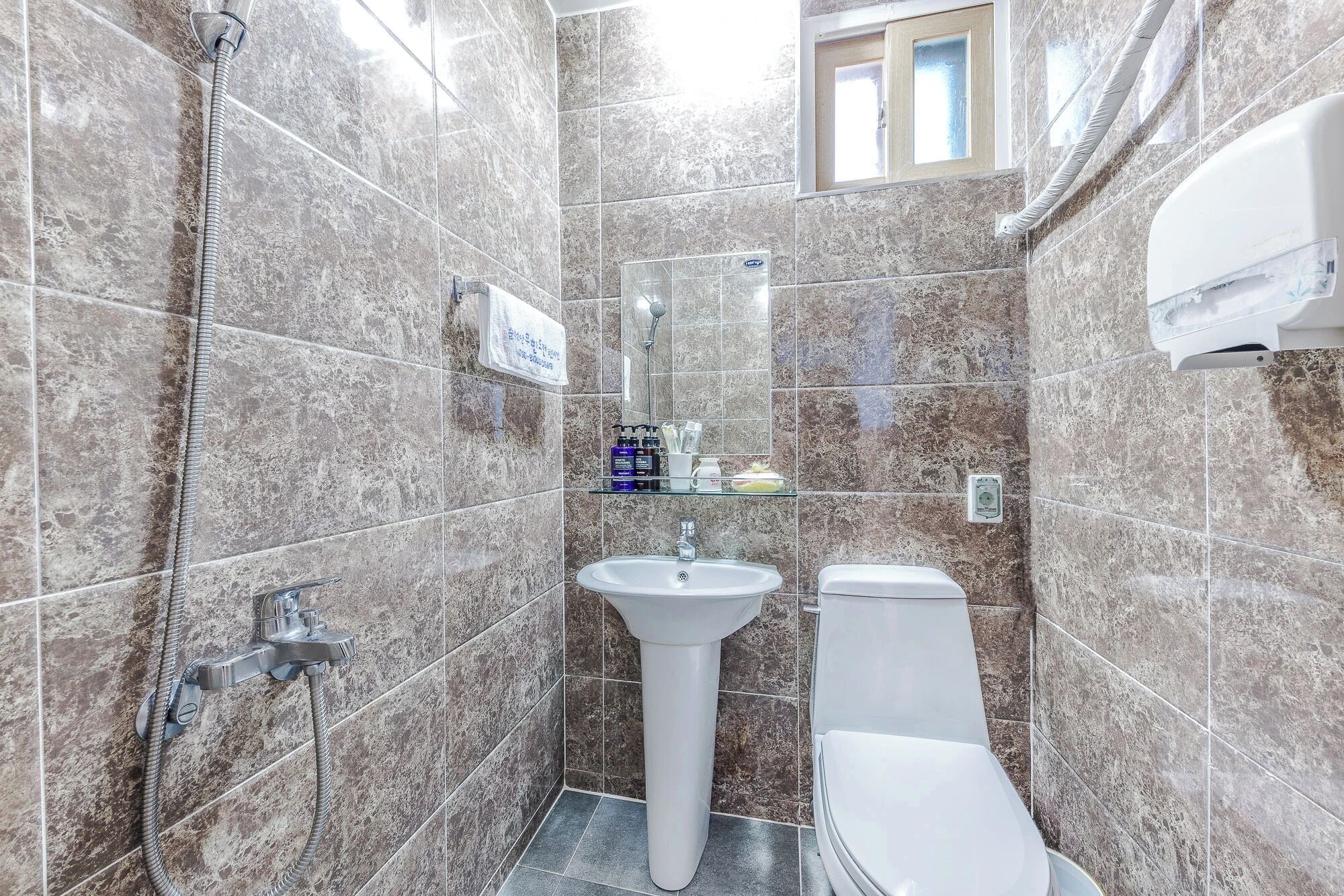 A bathroom with a shower, sink, toilet, and a glass shelf with toiletries.