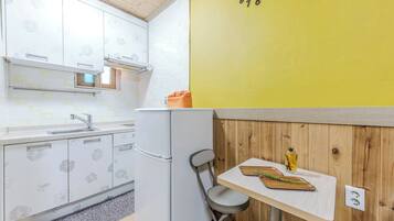 Een compacte keuken met een witte koelkast, een gootsteen en een houten wand met een gele klok.