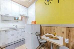 A compact kitchen with a white refrigerator, a sink, and a wooden wall with a yellow clock.