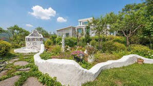 A garden with a white gazebo, a statue, and a house with a white fence.
