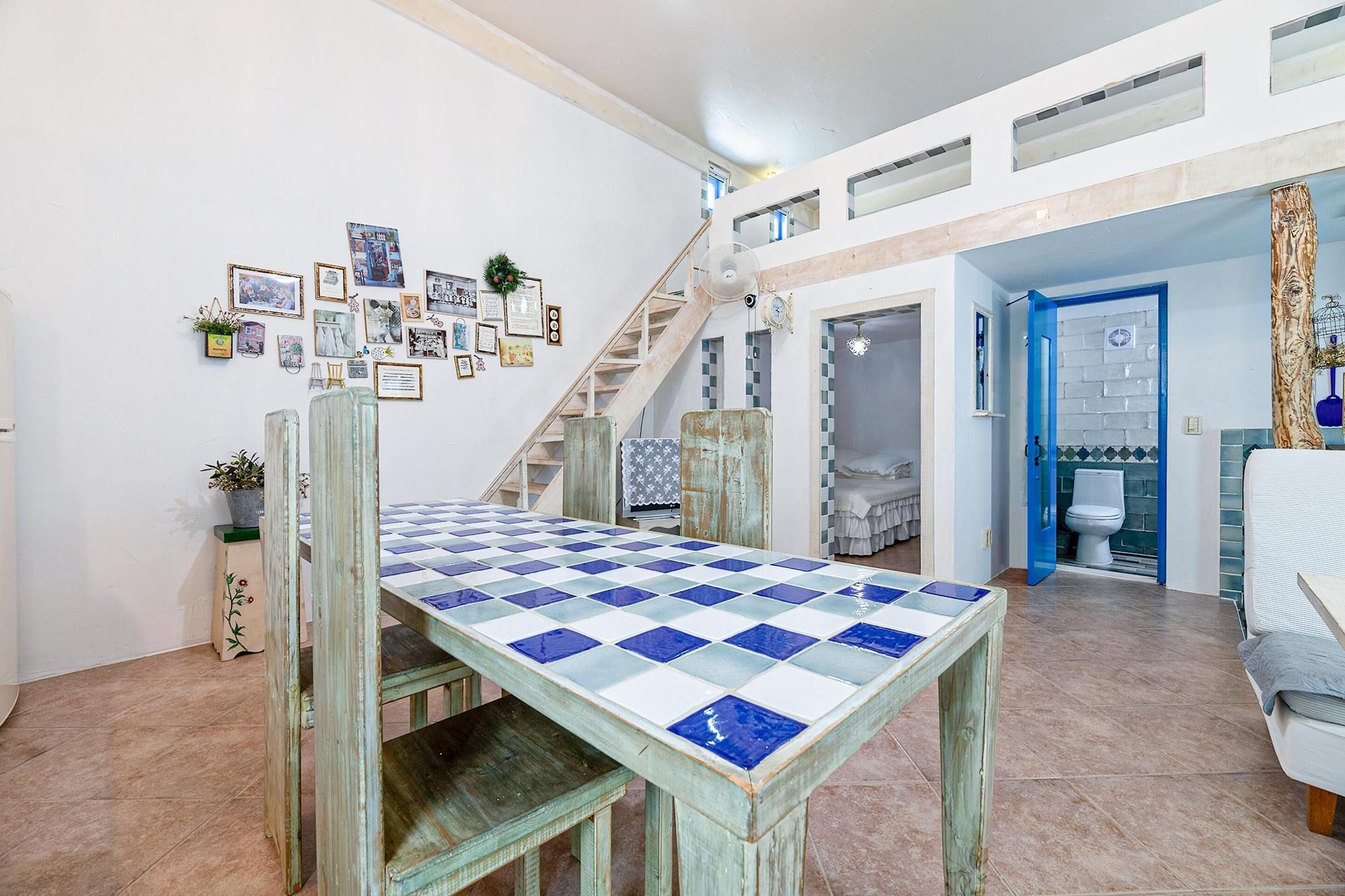 A spacious living area with a checkered table, a staircase, and a blue door leading to another room.