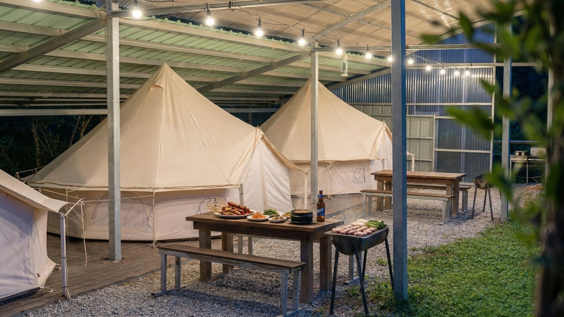 Un terrain de camping avec deux tentes, une table avec de la nourriture et un barbecue.