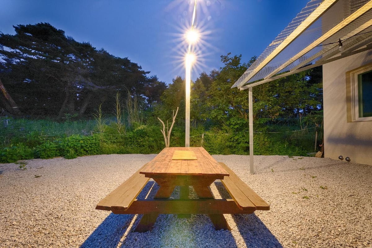 Una mesa de picnic de madera con banco, rodeada de grava, bajo una farola.