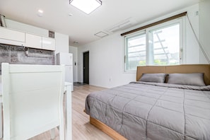 Un dormitorio con cama, ventana con vistas, kitchenette y puerta que da a otra habitación.