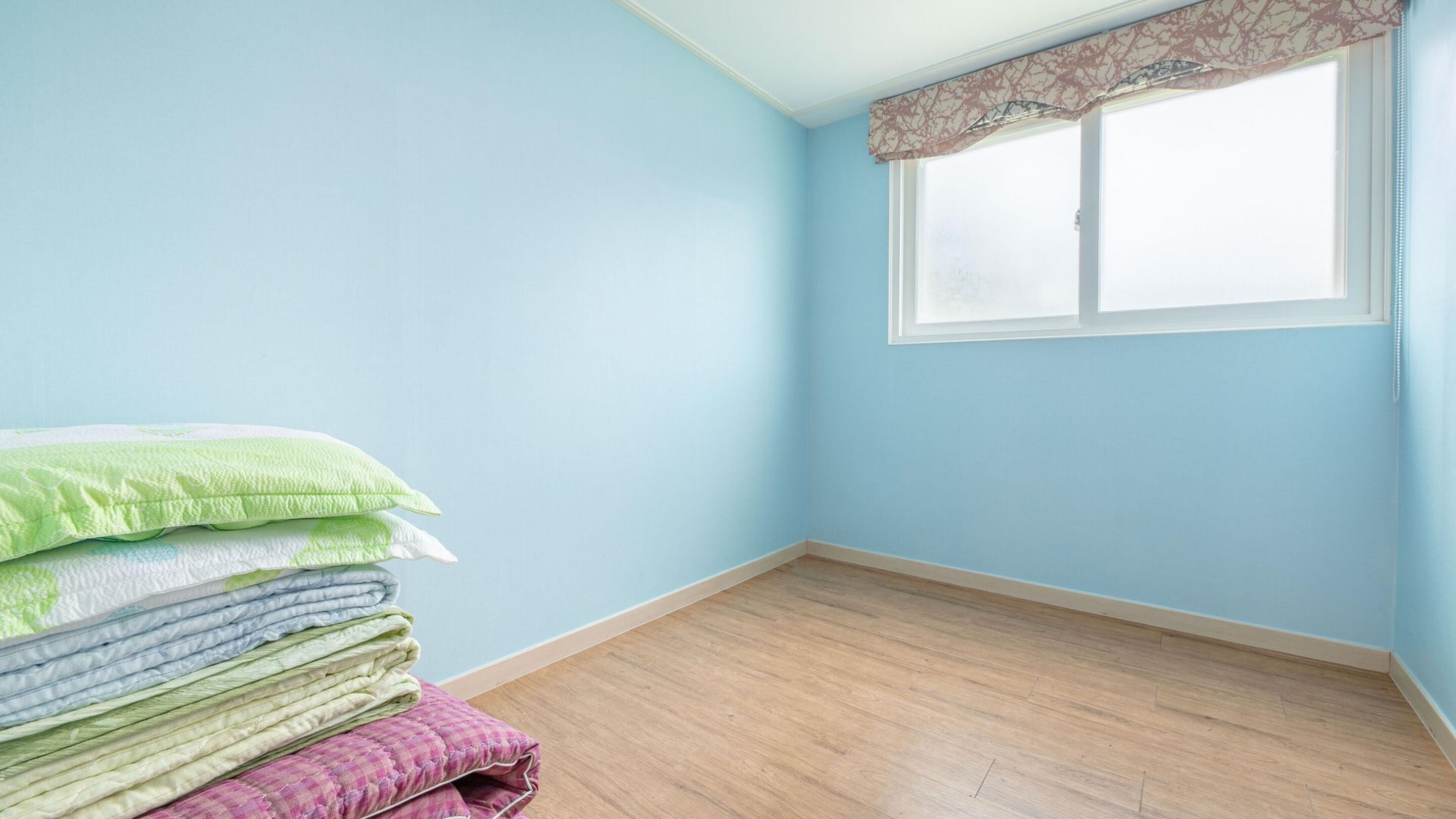 A room with light blue walls, a wooden floor, and a window with a patterned valance.