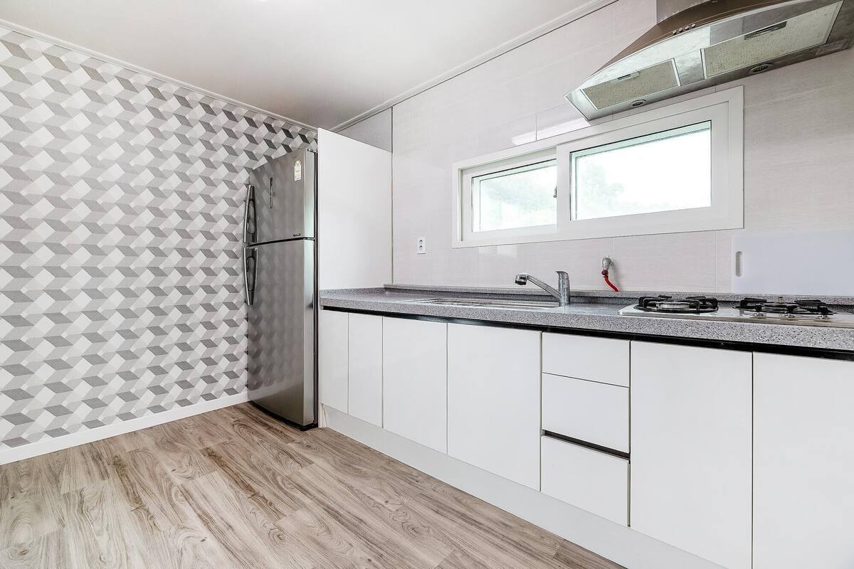 A modern kitchen with a stainless steel refrigerator, a gas stove, white cabinets, and a patterned wall.