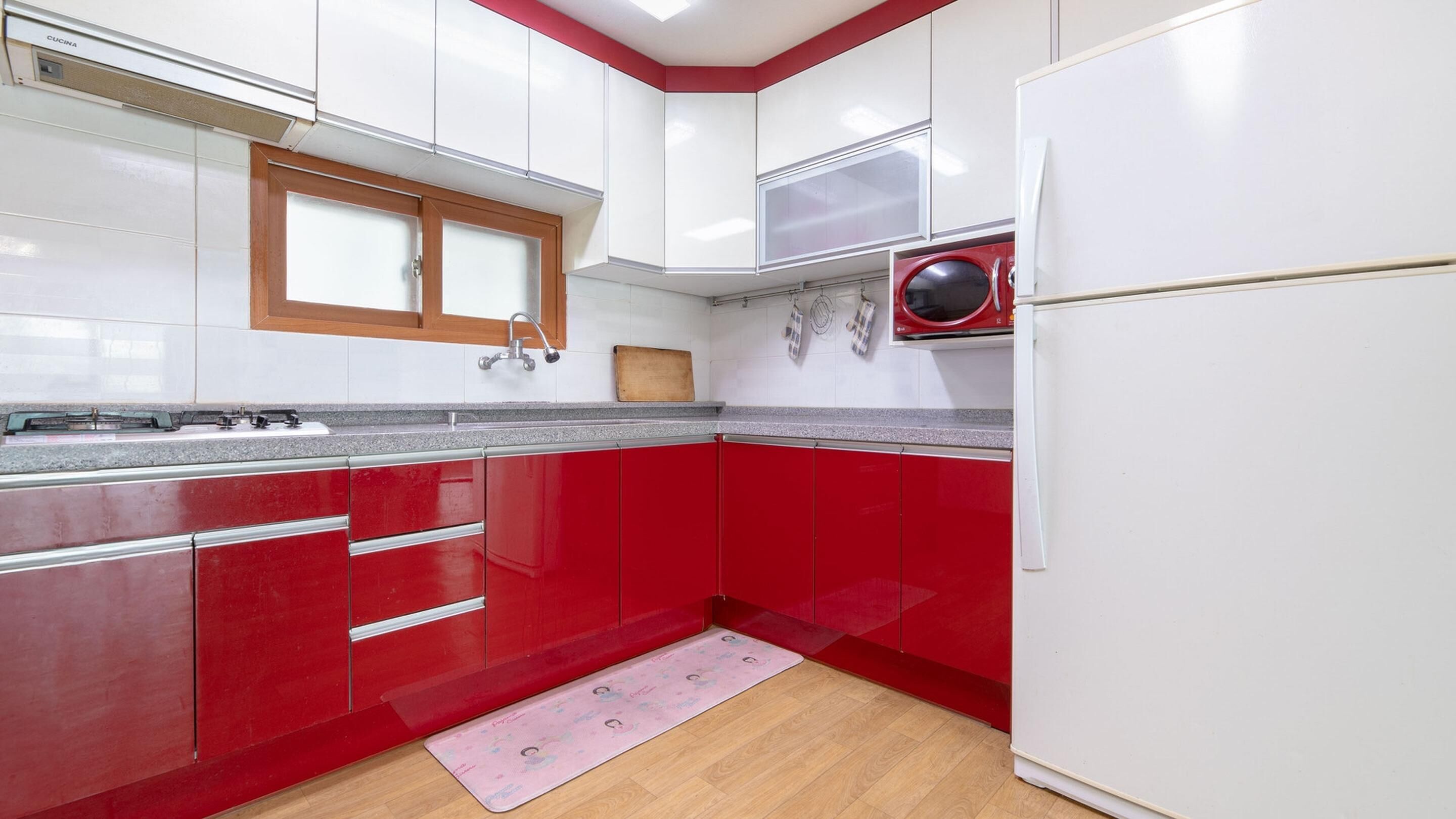 A kitchen with red and white cabinets, a microwave, and a wooden window above the sink.