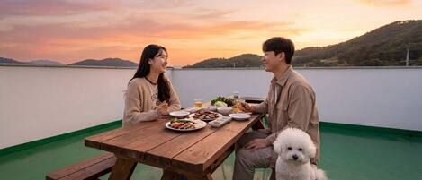 A couple dining at a wooden table with a view of a lake and hills during sunset.