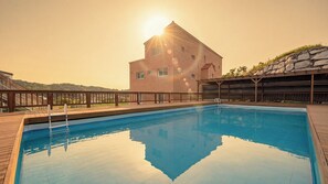 Una piscina con cubierta de madera, un edificio de ladrillo al fondo y cielo despejado.