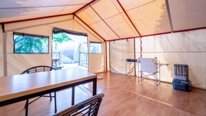 Une pièce aménagée avec une tente, une table et des chaises en bois, un tableau blanc et un radiateur portatif.
