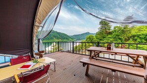 Un pontile in legno con tavolo e sedie, vista su un corpo d'acqua e dolci colline.