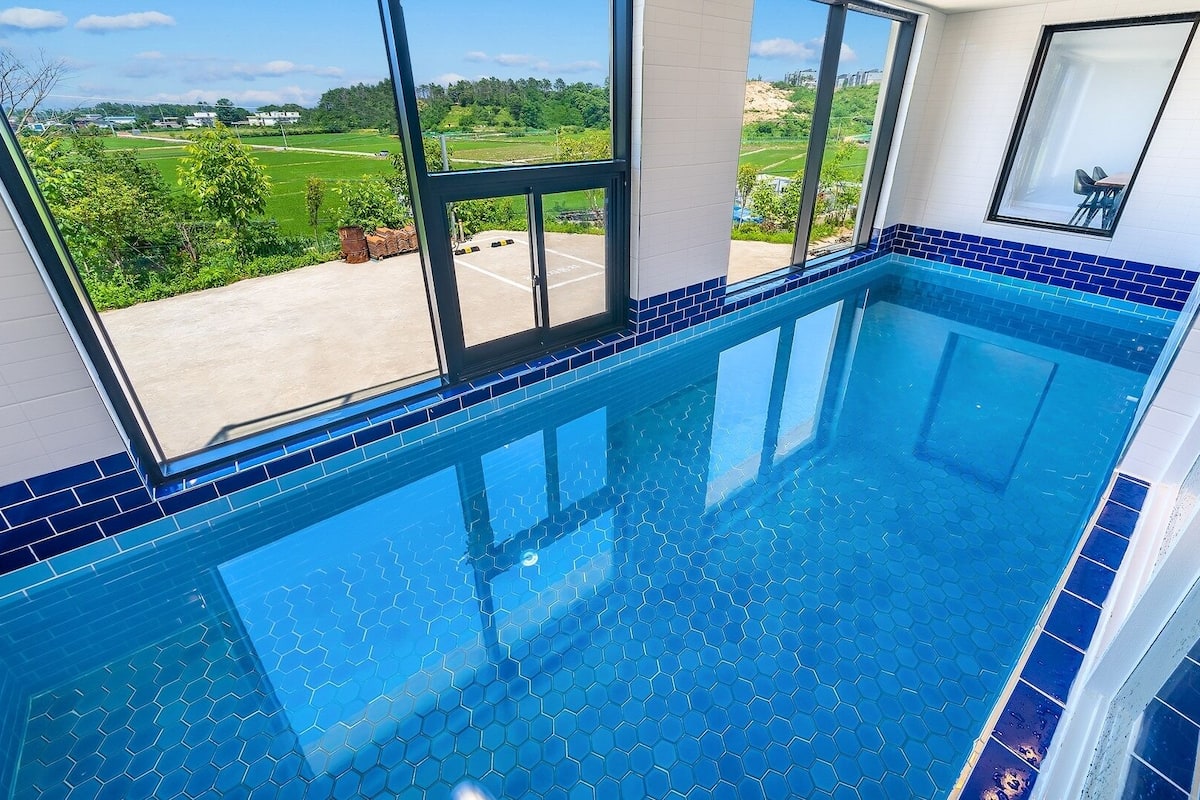 A swimming pool with a view of a green landscape through large windows.