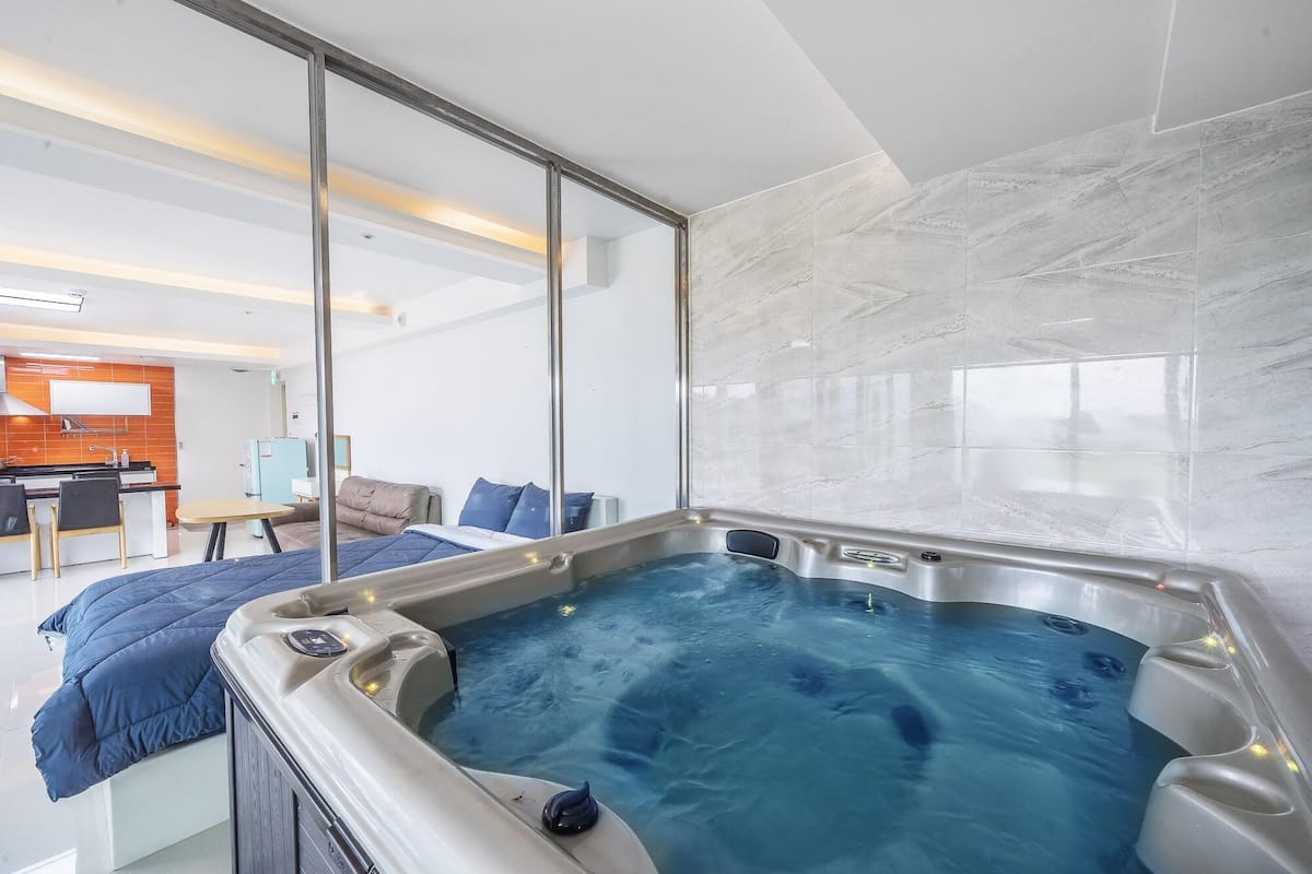 A modern room with a large hot tub, a sofa, and a dining area.