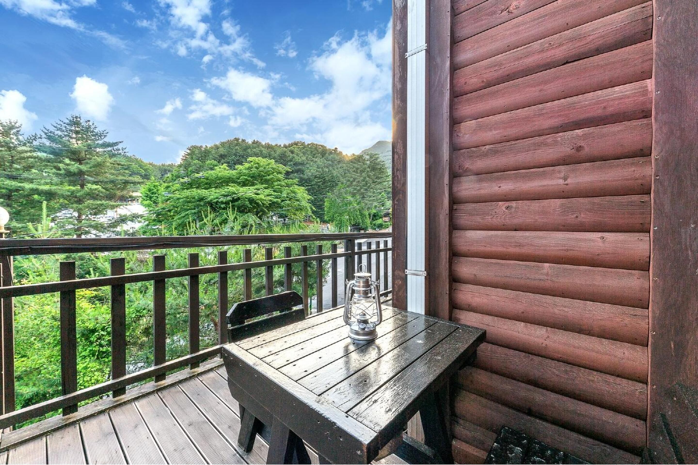 A wooden deck with a table and a lantern, overlooking a forested area.