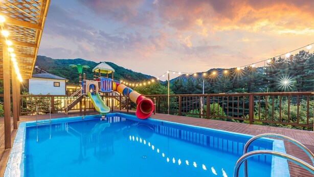 Ein Schwimmbad mit Rutsche, einer Holzterrasse und Lichterketten.