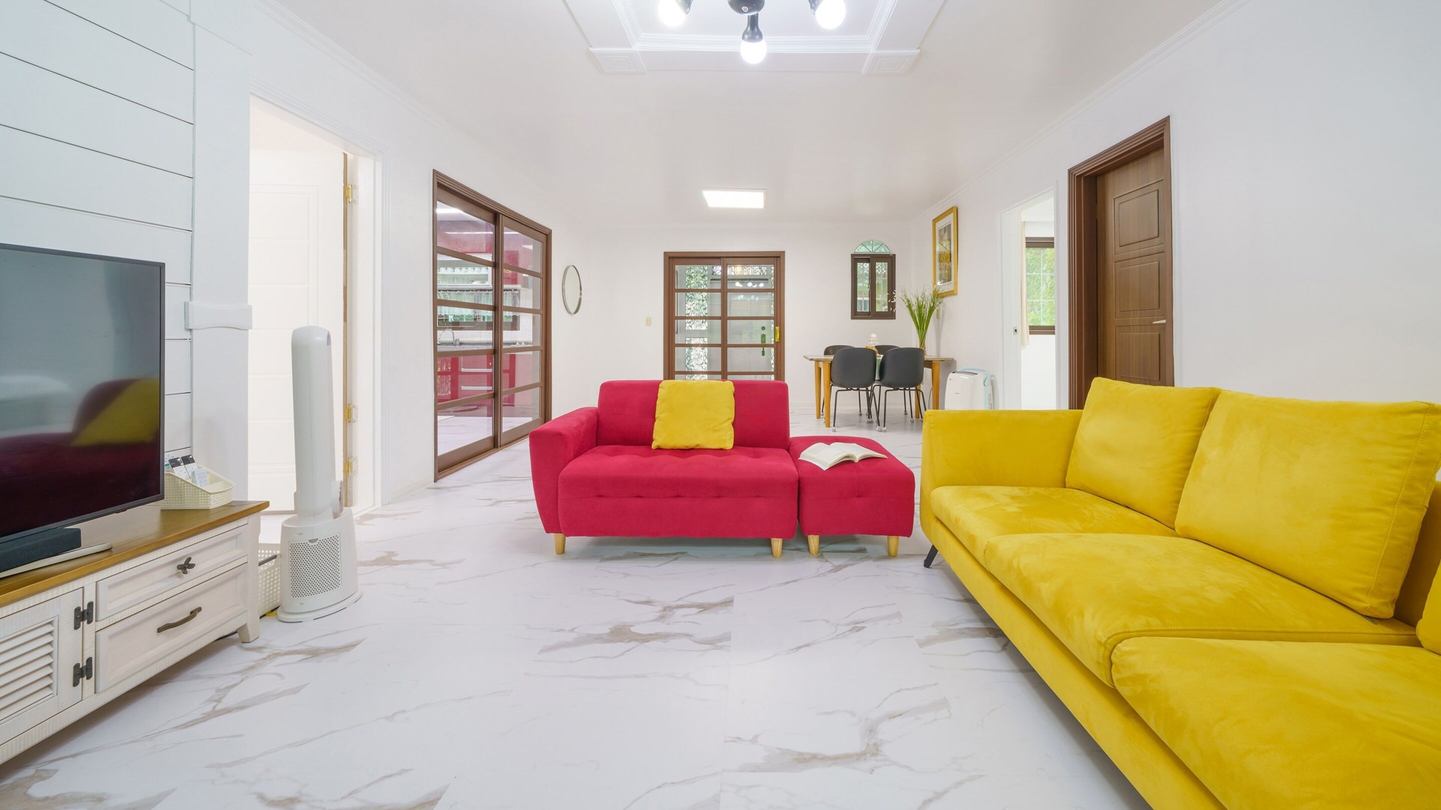 Una sala de estar con televisor, un sofá rojo, un sofá amarillo y un comedor con sillas y una mesa.