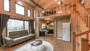 Ein Holzblockhaus-Interieur mit Sofa, Esstisch, Küche und einer Schlafgalerie.