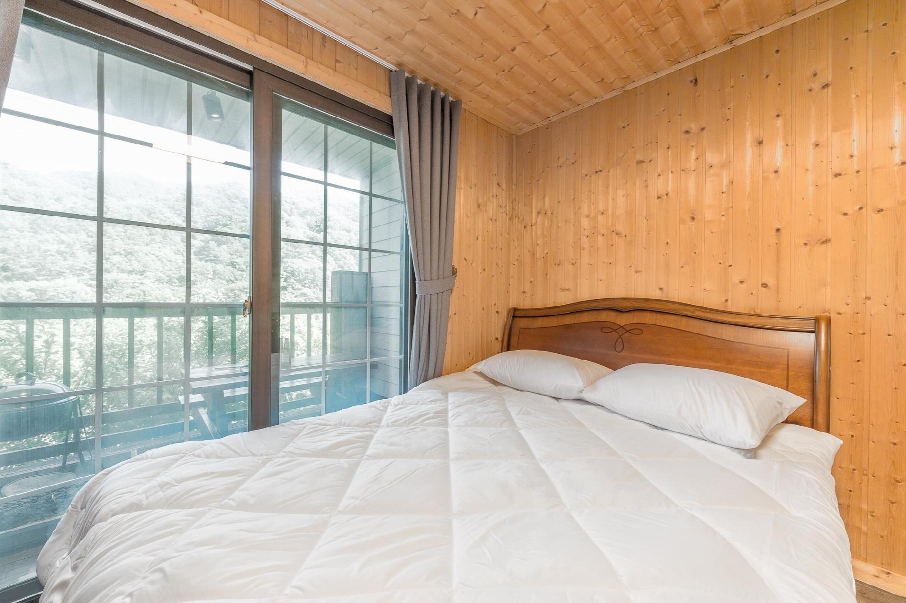 Ein Schlafzimmer mit einem hölzernen Kopfteil, einem großen Fenster mit Vorhängen und Blick auf einen Balkon.