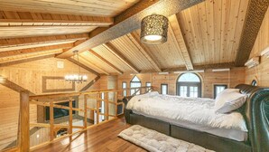 Ein Holzhütten-Innenraum mit Schlafzimmer im oberen Bereich, einer Treppe und einem großen Fenster.