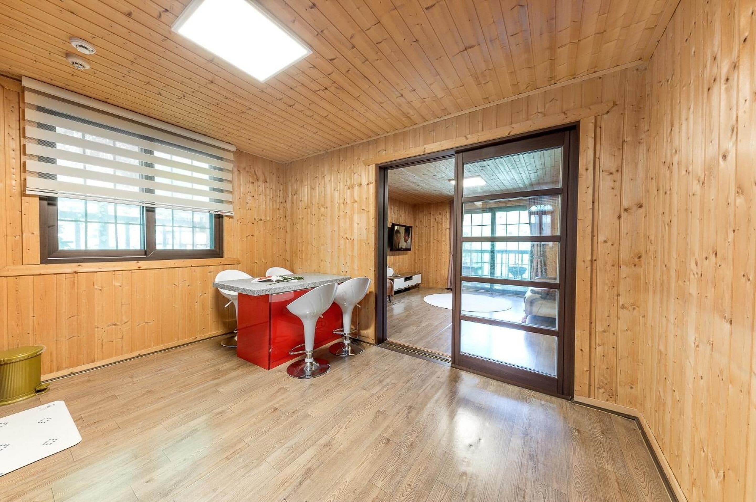 A wooden-paneled room with a bar area, a sliding glass door leading to a balcony, and a large window with blinds.