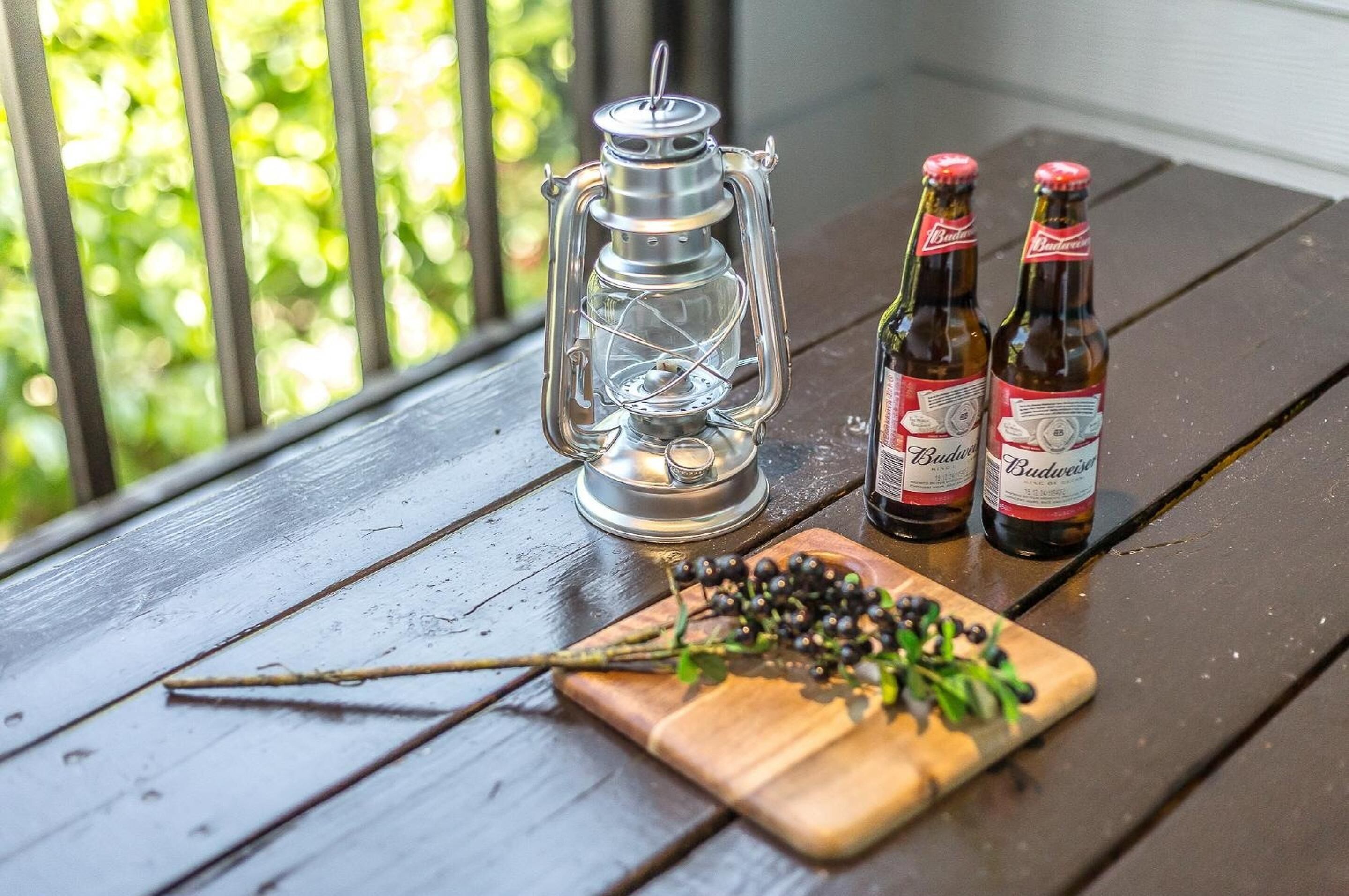A wooden table with a lantern, two Budweiser beer bottles, and a branch with berries.