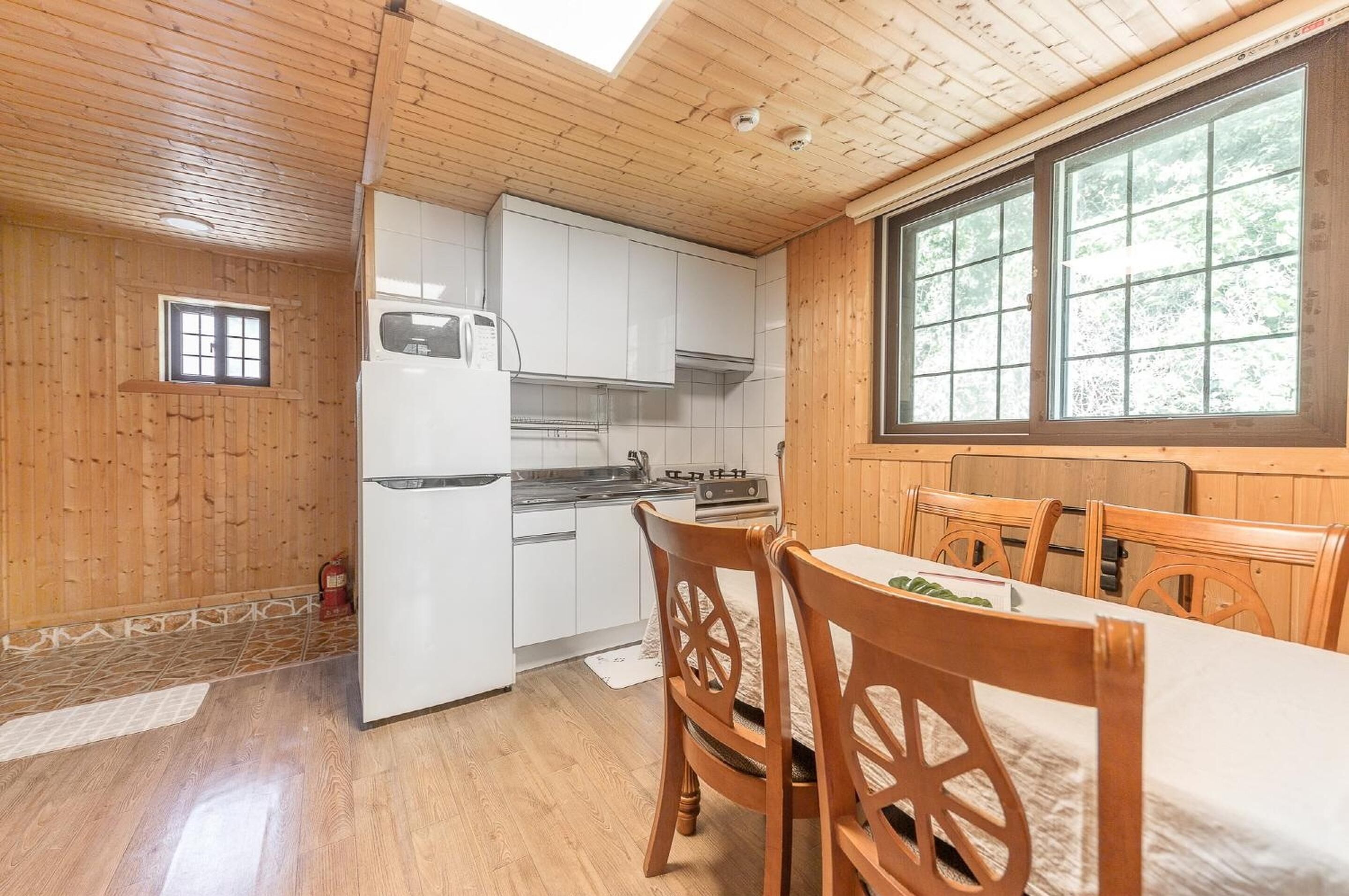 Une cuisine compacte avec des meubles blancs, un réfrigérateur et un coin repas comprenant des chaises et une table en bois.